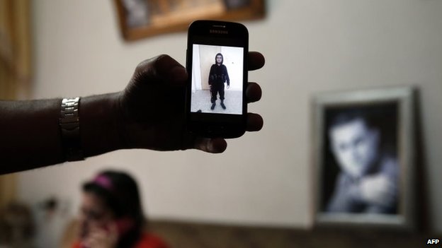 The brother of Mohammed Musallam holds a phones showing a photograph of him dressed in black, military fatigues in Syria